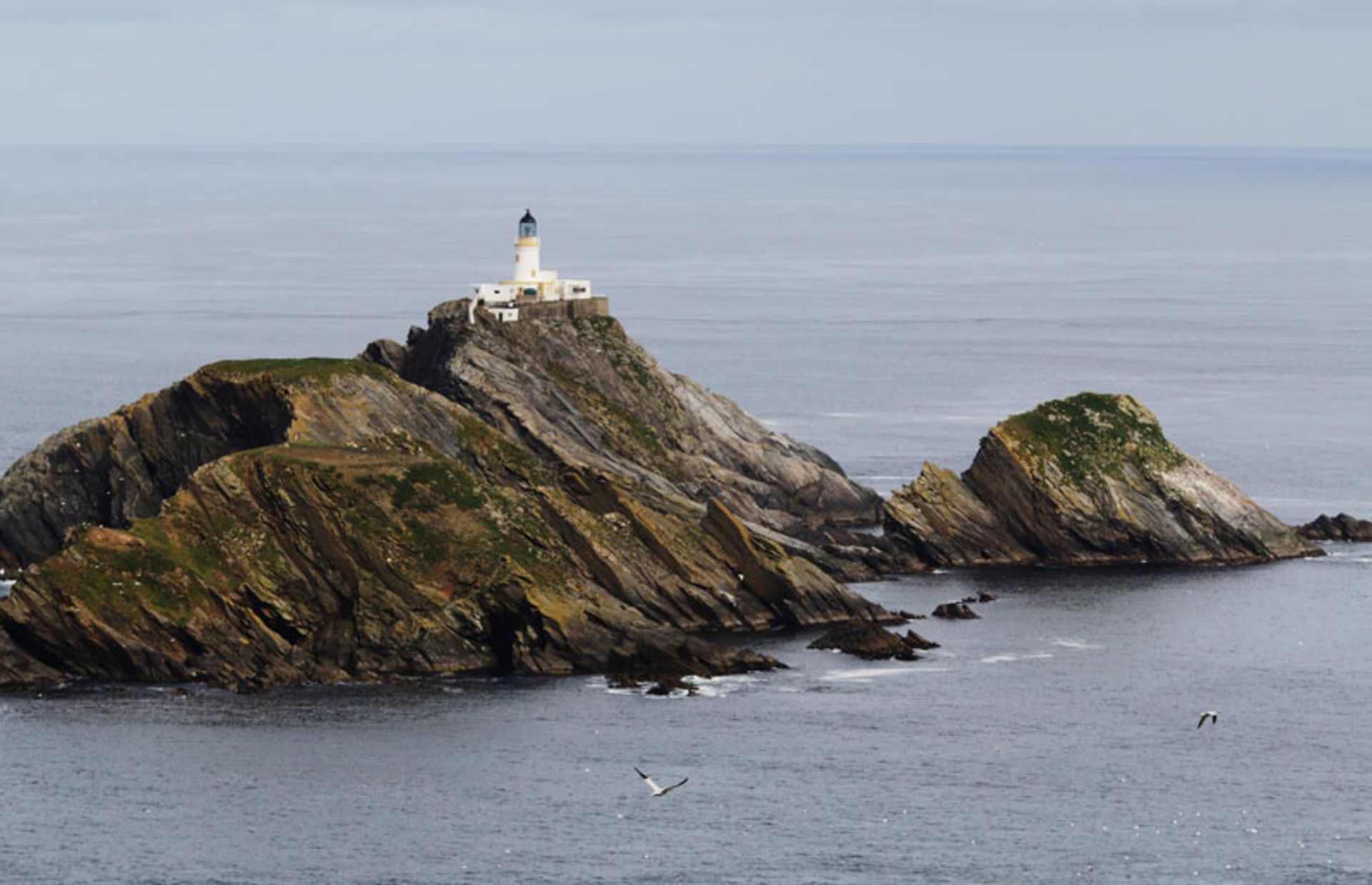 فانوس دریایی سفید بر فراز صخره‌های تیز در میان دریا