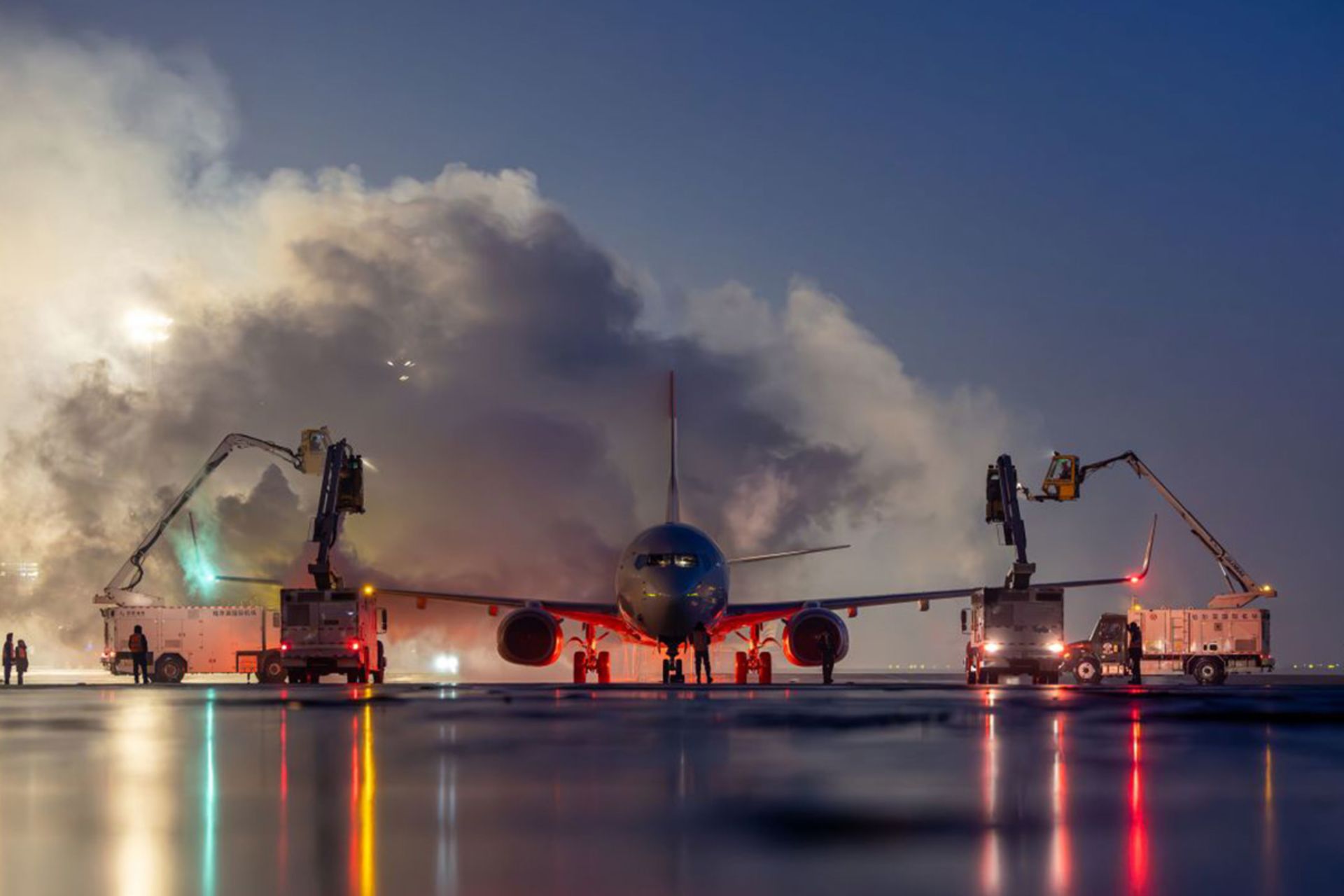 چندین دستگاه یخ‌زدا دور یک هواپیما با انعکاس نور در باند خیس