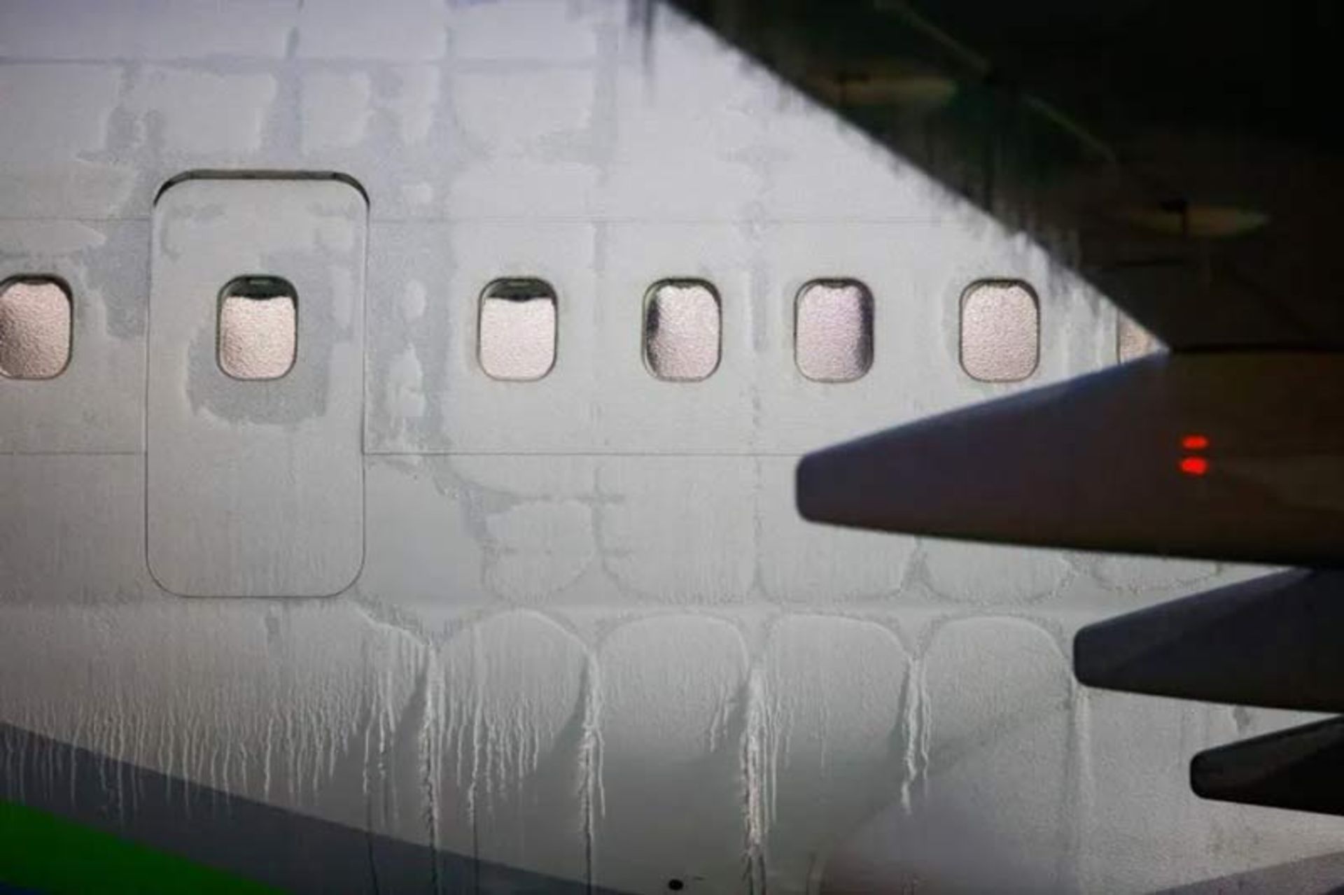 نمای نزدیک از پنجره‌های یخ‌زده هواپیما و آثار ذوب شدن برف روی بدنه