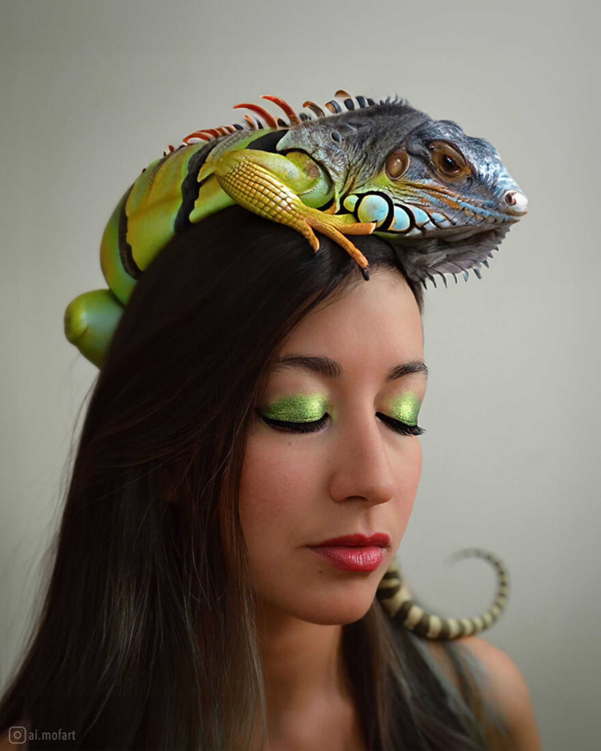 زنی با آرایش چشم سبز و طلایی که یک ایگوانا روی سر