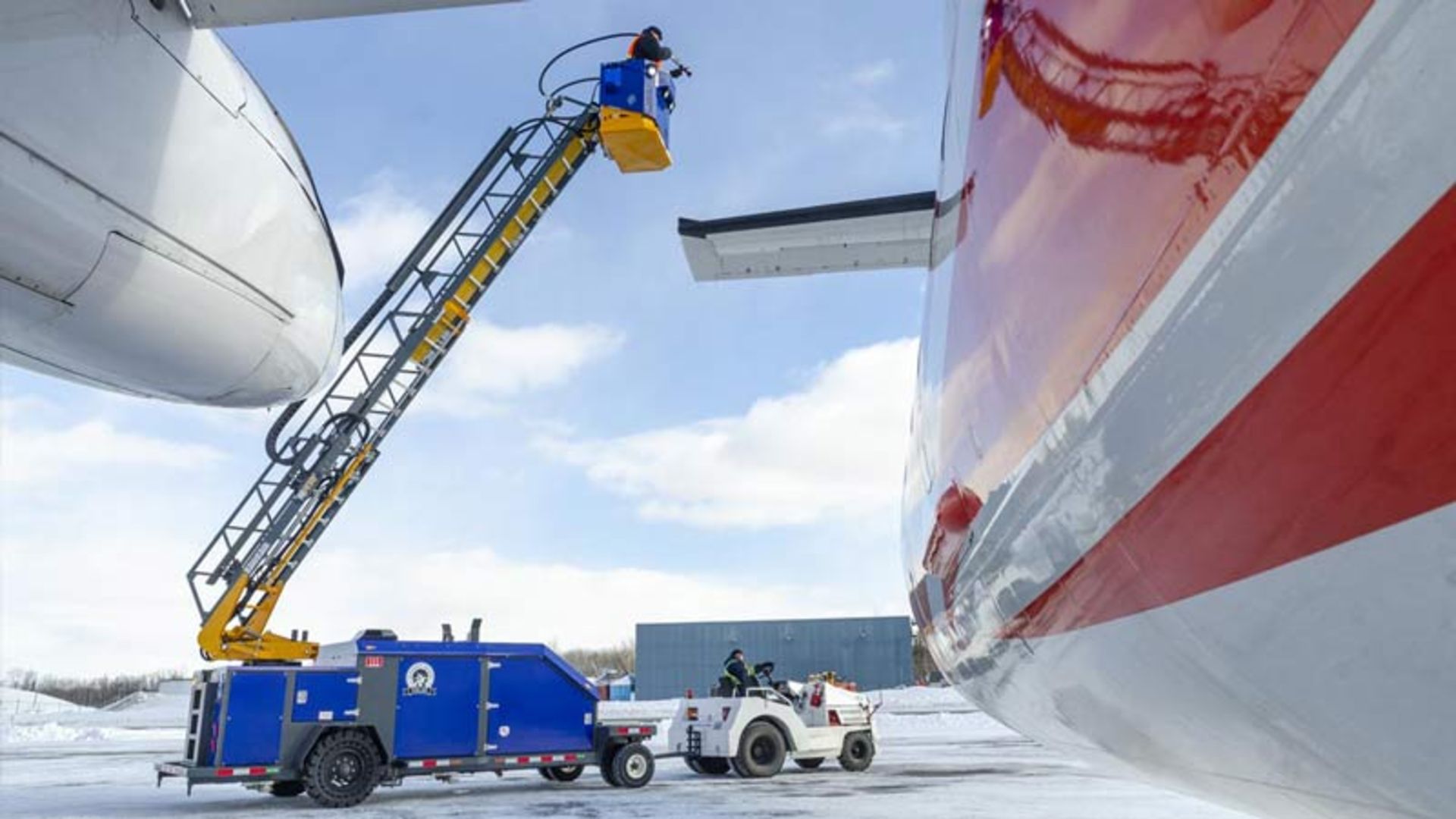 اپراتور در سبد بالابر در حال یخ‌زدایی از بخش‌های بالایی هواپیما در محیطی برفی