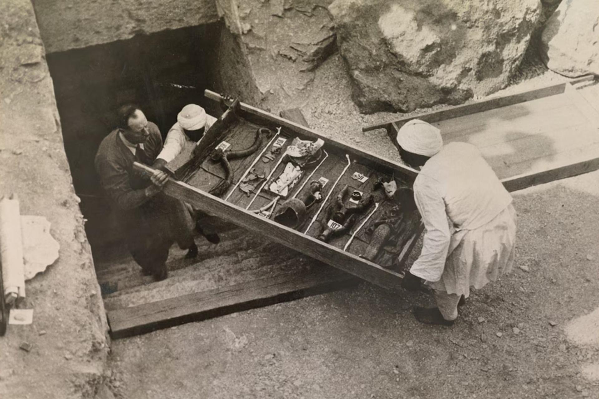 باستان‌شناس و کارگران در حال حمل یک سینی قطعات کوچک گنجینه از پله‌های ورودی مقبره