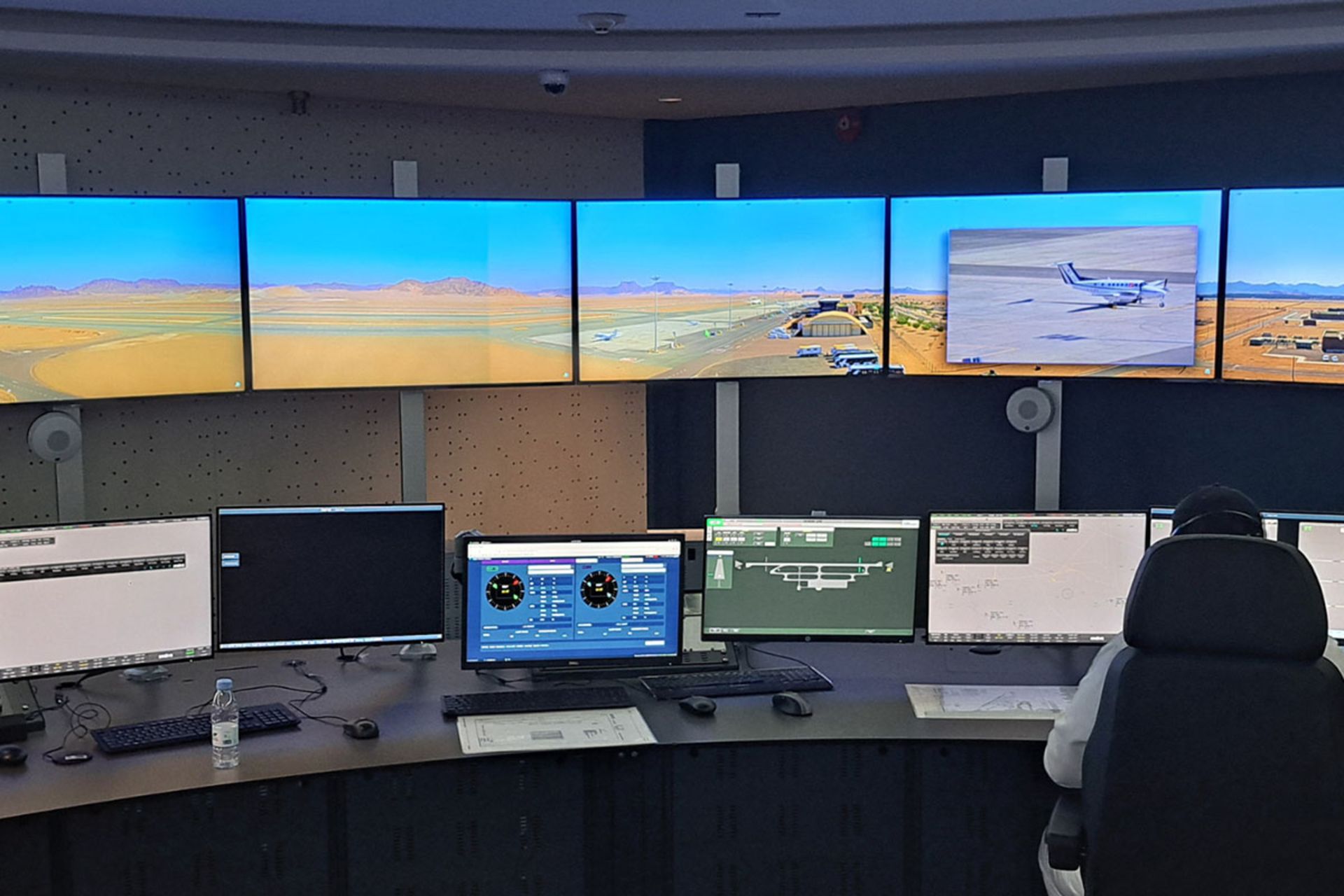 یک اپراتور در مقابل ردیفی از مانیتورهای عریض از داخل مرکز کنترل از راه دور فرودگاه بین‌المللی العُلا