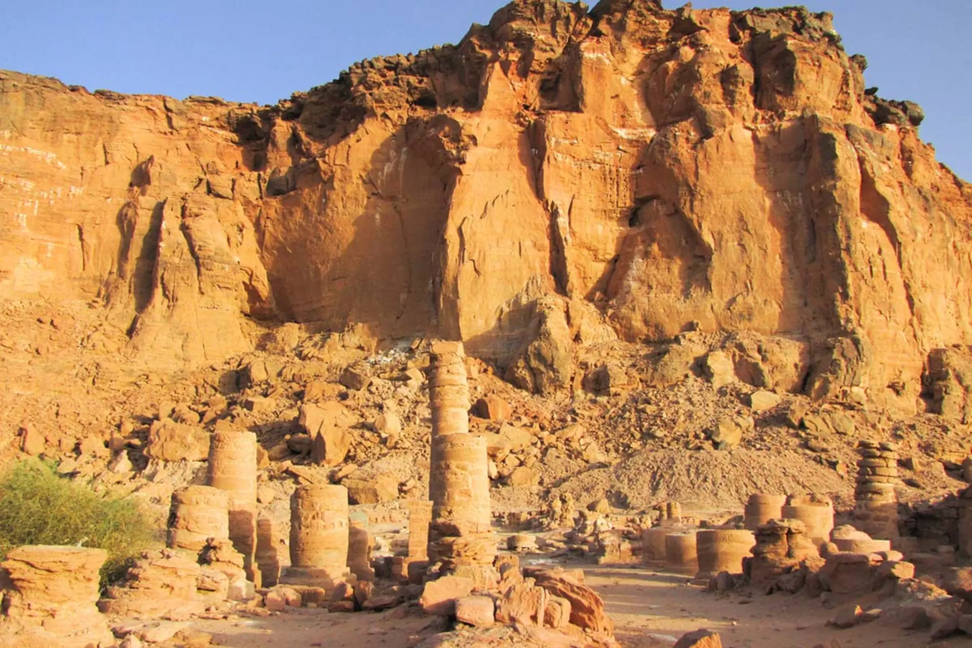 نمای صخره‌های بلند و نارنجی‌رنگ در صحرای سودان به همراه بقایای ستون‌های سنگی کوتاه