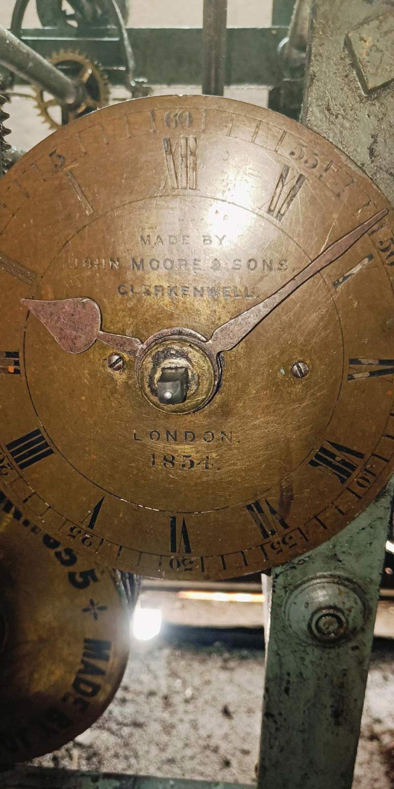 نمای نزدیک از صفحه برنجی و قدیمی ساعت که نام سازنده و سال ساخت روی آن حک شده 